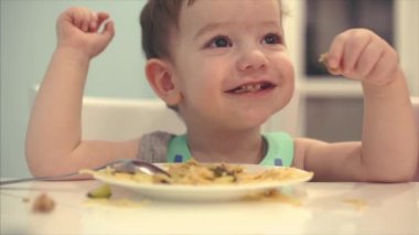 Küçük çocuk bir önlük bir masada oturan ve kendi spagetti yemek bebek yiyor isteyerek.