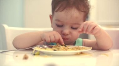 Küçük çocuk bir önlük bir masada oturan ve kendi spagetti yemek bebek yiyor isteyerek.