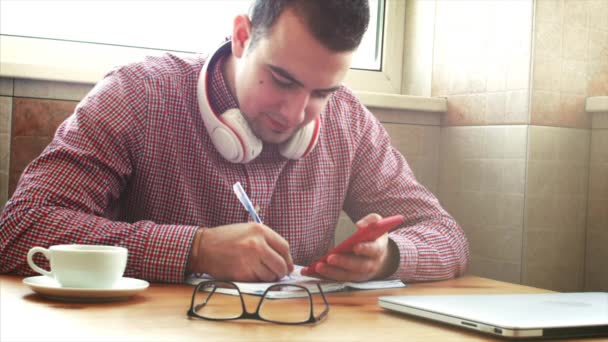 Молодой бизнесмен, сидящий за столом и пьющий кофе, делает работу, пишет в книге. Бизнесмен пишет домашнее задание. Съемка . — стоковое видео