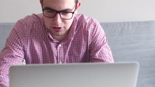 Молодой человек, сидящий за столом и пьющий кофе, разговаривающий с другом по видеосвязи на компьютере . — стоковое видео