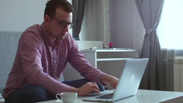 Mladý muž, sedící u stolu pití kávy, kterou si kamaráda na audiovizuální volání v počítači. — Stock video