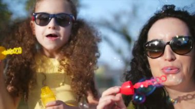 Mutlu aile gülümseyen, anne ve kızı, yaz aylarında açık sabun köpüğü üfleme oynuyorlar. Stok görüntüleri.