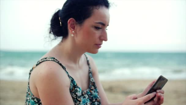 Mujer joven caucásica usando teléfono inteligente junto al mar . — Vídeo de stock