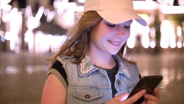 Atractiva adolescente usando un teléfono móvil mientras camina por las calles en una ciudad nocturna, en la ciudad nocturna de fondo. Material de archivo . — Vídeos de Stock