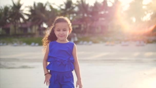 Молодая счастливая маленькая девочка, гуляющая у берега океана. Счастливая маленькая девочка в синем костюме, кавказская внешность, прогуливающаяся по берегу моря . — стоковое видео