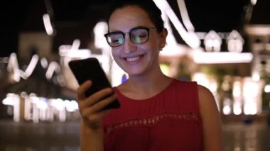 Çekici kız bir gece şehirde arka plan gece şehrin sokaklarında yürürken bir cep telefonu kullanarak. Stok görüntüleri.