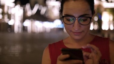 Çekici kız bir gece şehirde arka plan gece şehrin sokaklarında yürürken bir cep telefonu kullanarak. Stok görüntüleri.