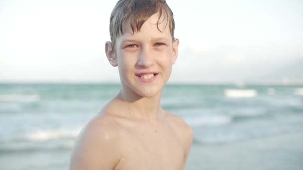 Close up, ritratto di un bel ragazzo adolescente che guarda la telecamera sorridente, spiaggia tropicale rallentata. Filmati di magazzino . — Video Stock