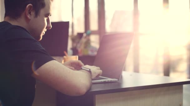 Joven hombre de negocios con gafas con un reloj en las manos, sentado en una mesa, haciendo trabajo en la computadora. 4K — Vídeo de stock