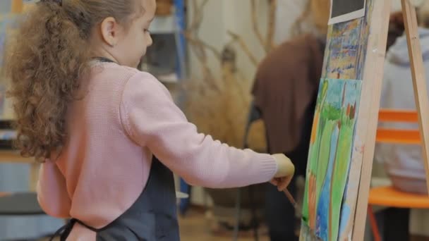 Junge Hände der Künstlerin, kleine Künstlerin bemalt eine Leinwand mit Pinsel, sitzt an einem Tisch und zeichnet auf Leinwand. Prozess des Zeichnens: im Künstleratelier Hand Baby Girl Skizzen auf Leinwand. — Stockvideo