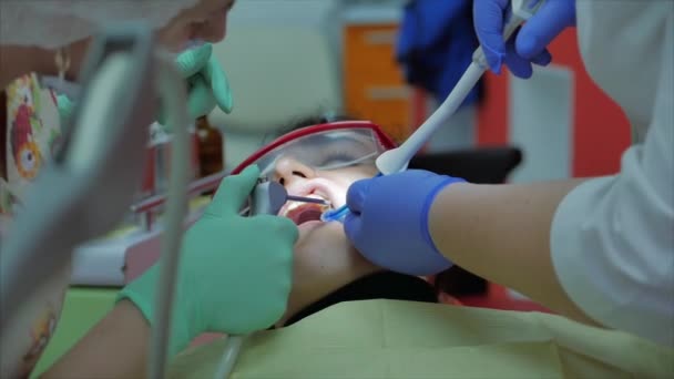 Mujer dentista tratando dientes a mujer paciente en clínica. Médico dentista profesional femenino en el trabajo, instala un relleno en un diente en el paciente deushka. Concepto de examen dental . — Vídeos de Stock