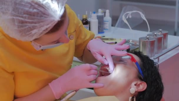 Kvinna tandläkare behandla tänder till kvinna patient på kliniken. Munhygien med en speciell lösning, rengöring av munhålan med ultra ljud. Kvinnlig professionell tandläkare på jobbet. Tandläkarundersökning — Stockvideo