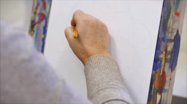 Sanatçının elleri, bir kadın sanatçı fırçayla bir tuval boyar, bir sehpaya oturur ve tuvale fırça darbeleri yapar. Çizim süreci: Sanat atölyesinde. Tablo üzerinde çizim.