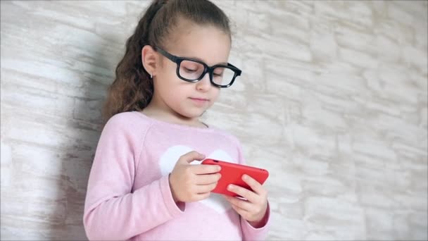 Aranyos baba szórakoztató egy mobiltelefon vagy tabletta. A kislány a szabadidejét egy mobil játékkal tölti, és a kezével összetöri a fényes képernyőt. Koncepció: Boldog gyermekkort, Játékok gyerekeknek. — Stock videók