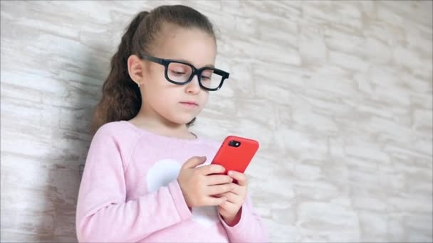 Leuke baby vermakelijk met een mobiele telefoon of tablet. Klein meisje besteedt haar vrije tijd aan het spelen van een mobiel spel en verplettert een helder scherm met haar hand. Concept: Happy Childhood, Games voor kinderen. — Stockvideo