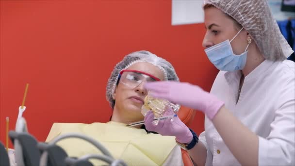 Zahnärztin behandelt Zahnpatientin in Klinik. Zahnärztin zeigt dem Patienten am Modell des Kiefers, wie man seine Zähne richtig behandelt, gibt Unterricht über die richtige Pflege der Zähne und der Mundhöhle — Stockvideo