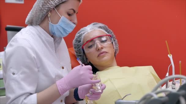 Дантист показывает пациентке модель челюсти, как правильно обращаться с зубами, дает уроки по правильному уходу за зубами и полостью рта — стоковое видео