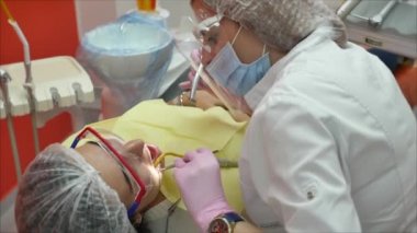 Profesyonel kadın diş hekimi klinikte dişlerini tedavi ediyor. Kadın profesyonel doktor stomatolog iş başında. Arkaplanda diş ekipmanı.