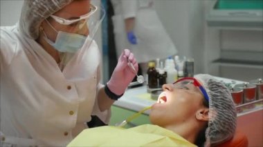 Profesyonel kadın diş hekimi klinikte dişlerini tedavi ediyor. Kadın profesyonel doktor stomatolog iş başında. Arkaplanda diş ekipmanı.