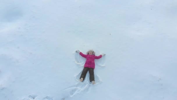 Šťastná dceruška dělá anděly ve sněhu. Happy, fun childhood on a Sunny winter day outdoors. — Stock video