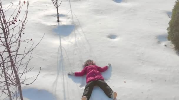 Šťastná dceruška dělá anděly ve sněhu. Happy, fun childhood on a Sunny winter day outdoors. — Stock video