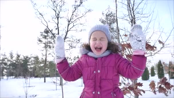 Feliz, divertida infancia en un soleado día de invierno al aire libre. Happy Little Girl mientras se divierte y sonríe mira a la cámara . — Vídeos de Stock