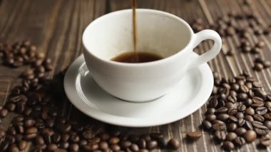 Kahve fincanı ve kahve çekirdeği. Masanın üzerinde kavrulmuş fasulyeyle buharlaşan bir fincan kahve. Slow Motion kahve doldur..
