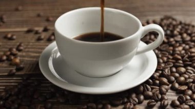 Kahve fincanı ve kahve çekirdeği. Masanın üzerinde kavrulmuş fasulyeyle buharlaşan bir fincan kahve. Slow Motion kahve doldur..