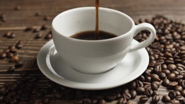 Taza de café y granos de café. Taza blanca de café evaporando sobre la mesa con frijol asado. Slow Motion café verter . — Vídeo de stock