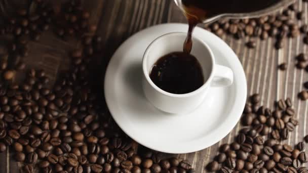 Coffee cup and coffee beans. White cup of evaporating coffee on the table with roasted bean. Slow Motion coffee pour. — Stock Video