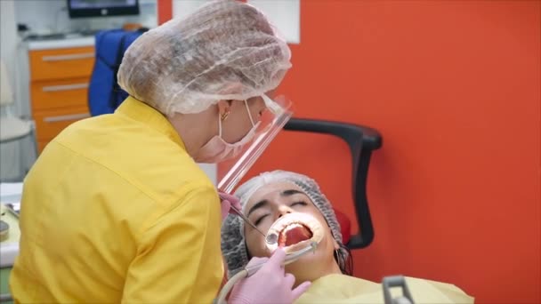 Persoon ondergaat een medisch onderzoek en behandeling van de mondholte bij de tandarts. Tandarts trakteert vrouwen op een patiënt in de kliniek. Vrouwelijke professionele dokter Stomatoloog op het werk. — Stockvideo