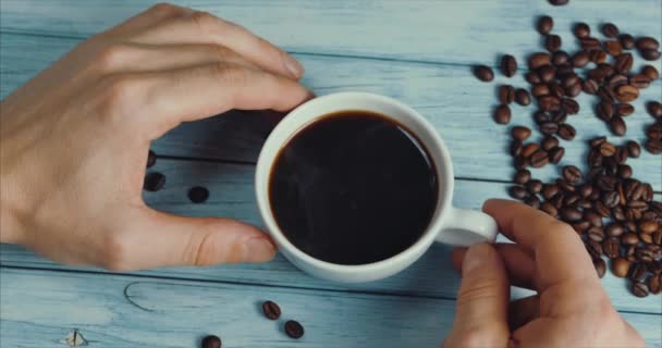 Männliche Hand nimmt eine Tasse Kaffee und Kaffeebohnen. weiße Tasse dampfenden Kaffees auf dem Tisch mit gerösteten Bohnen.