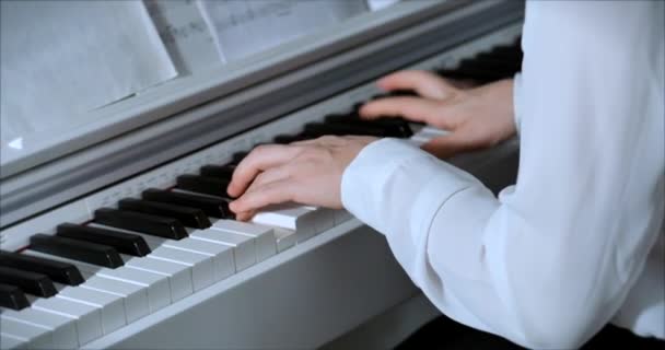 女性または少女学生またはプロのピアニストは、美しい白いピアノでクラシック音楽を演奏し、ピアニストの手はスローモーションで閉じます。ピアノキーは暗い色で閉じます。4k — ストック動画