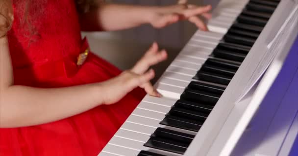 Little Baby Girl of Child Professional Pianist speelt klassieke muziek op een mooie witte piano een kerstvakantie tegen de achtergrond van een kerstboom en knipperende nieuwjaarslichten. Pianisten handen — Stockvideo