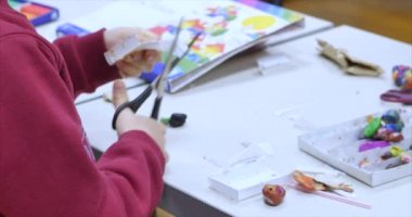 Sanat atölyesinde çalışan genç bir sanatçı ya da çocuk masaya oturur ve kağıt makasla bir figür keser. Öğrenme süreci ya da çocuk yaratıcılığı atölyesi, el işi. 4k