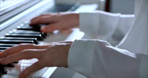 Frau oder Studentin oder professionelle Pianistin spielt klassische Musik auf einem schönen weißen Piano an einem Weihnachtsfeiertag vor dem Hintergrund eines Weihnachtsbaums und blinkender Silvesterlichter. Pianistenhände. — Stockvideo