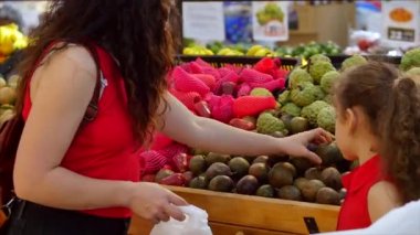 Pretty young Woman or Mother and Child or daughter buys food, vegetables, avocado, fruits, carrots, cabbage, salad, cauliflower, meat, apples, tomatoes, oranges in the market, in the supermarket.