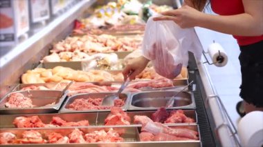 Kadın et alıyor, tavuktaki et parçalarına bakıyor markette, markette maşayla et topluyor..