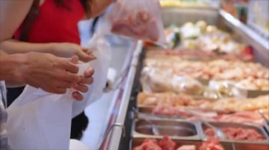 Buyers in the supermarket in the meat department are picking meat in bags to weigh and make a purchase. People buy meat, look at pieces of meat, pick up pieces of meat with tongs at the supermarket.