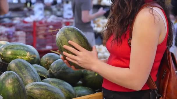 Pretty young woman or mother makes purchases in a supermarket, chooses food watermelon, avocado, fruits, carrots, cabbage, salad, cauliflower, meat, apples, tomatoes,oranges in the market,supermarket. — ストック動画
