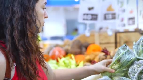 Pretty young beautiful girl or woman buys food, vegetables broccoli or cauliflower, fruits, carrots, cabbage, salad, cauliflower, meat, apples, tomatoes, oranges in the market, in the supermarket. — Stockvideo