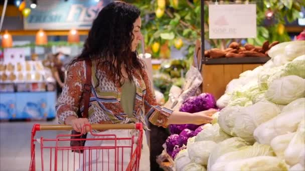 Rapariga bonita ou mulher faz compras em um supermercado compra comida, estilo de vida saudável, escolhe tomates saudáveis, cenouras, repolho, alface, no mercado, no supermercado. Compras . — Vídeo de Stock