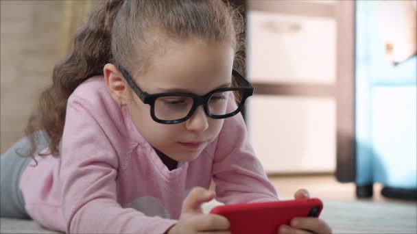 Leuke baby vermakelijk met een mobiele telefoon of tablet. Klein meisje besteedt haar vrije tijd aan het spelen van een mobiel spel en verplettert een helder scherm met haar hand. Concept: Happy Childhood, Games voor kinderen. — Stockvideo