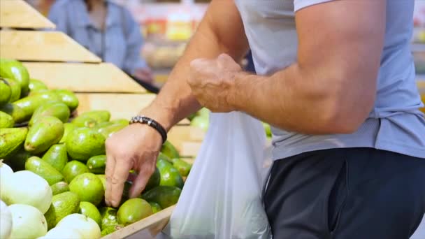 Homem saudável muito forte compra alimentos, frutas, abacates, está fazendo compras no supermercado, escolhendo produtos no supermercado para cozinhar, alimentos saudáveis, tomates, abacates, frutas, laranjas em — Vídeo de Stock