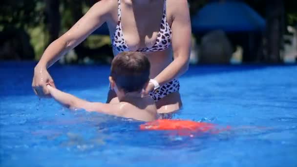 Mamá o una niñera-entrenador sostiene a su hijo en sus brazos, lo abraza, enseña a nadar. El niño sonríe felizmente. Baby Boy nadar en la piscina . — Vídeo de stock