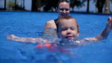 Mutlu anne ve küçük oğlu bodrumda yüzerek vakit geçiriyorlar. Küçük çocuk mutlu bir şekilde havuzda yüzüyor..
