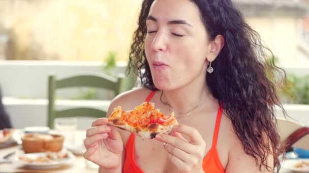 Joven linda mujer de aspecto italiano en un vestido rojo comiendo con impaciencia y disfrutando de la pizza italiana mientras está en un restaurante. El concepto de comida femenina, nutrición, calorías . — Vídeo de stock