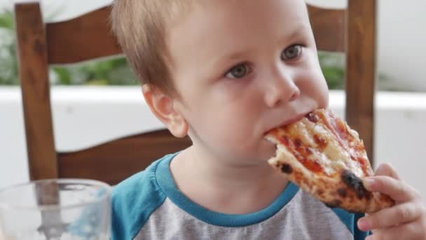 Bonito menino pré-escolar saudável comendo pizza italiana enquanto sentado em um café de crianças. Criança feliz come ansiosamente e gosta de pizza italiana em um restaurante. Infância, conceito de saúde . — Vídeo de Stock