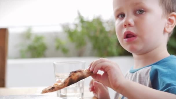 Lindo niño preescolar saludable comiendo pizza italiana mientras está sentado en un café para niños. El niño feliz come con entusiasmo y disfruta de la pizza italiana en un restaurante. Infancia, concepto de salud . — Vídeo de stock