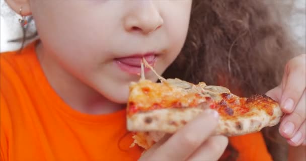 Young Little Caucasian Girl con trenzas se come con impaciencia una pizza pedazo. Encantadora joven feliz risa y morder gran rebanada de pizza recién hecha. Concepto alimentario internacional. De cerca. . — Vídeo de stock